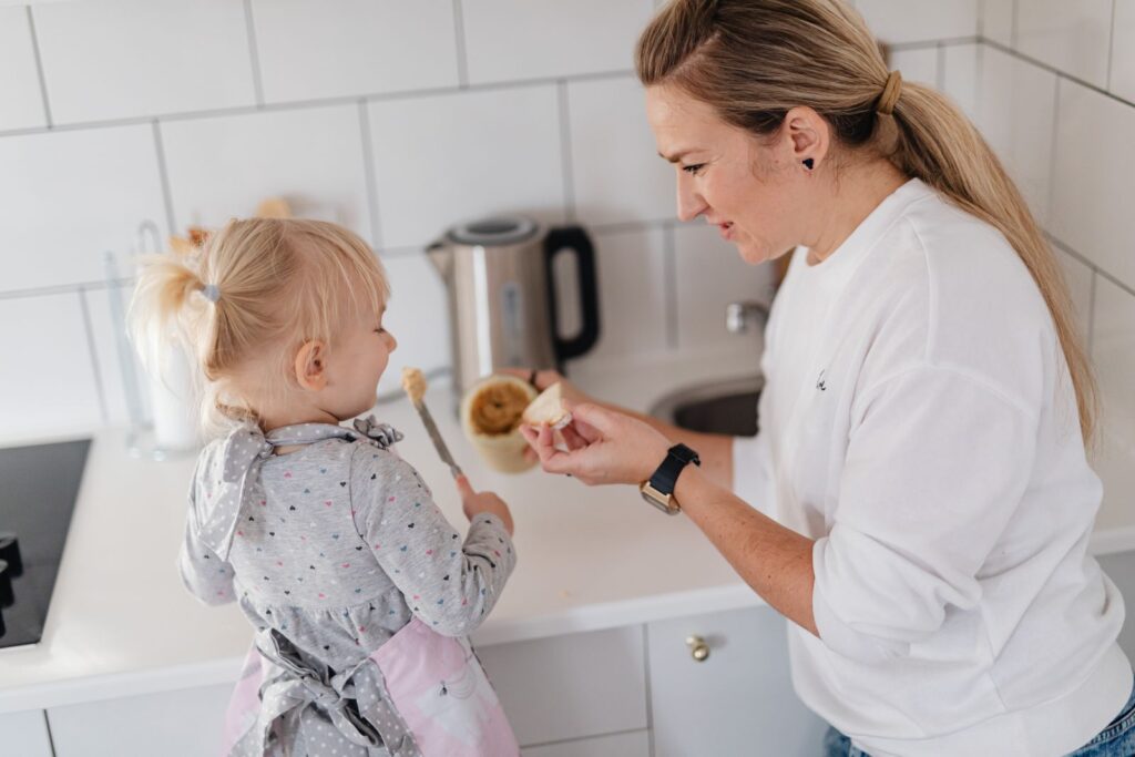 A mother and her young daughter interact while preparing food in a modern kitchen.