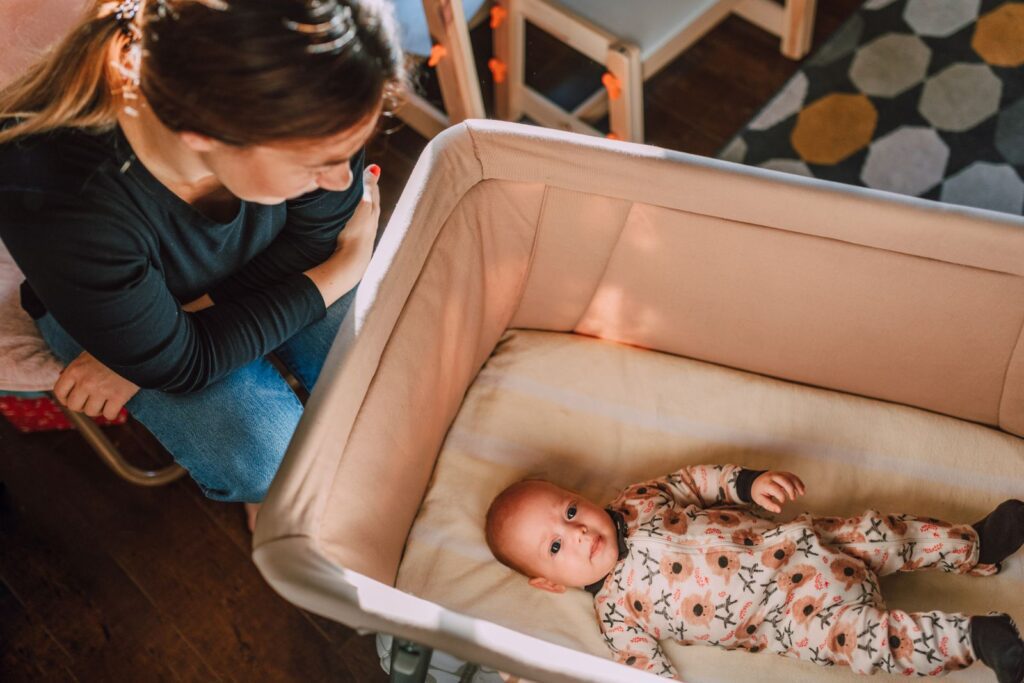 A mother lovingly watches over her baby in a crib from an overhead view.