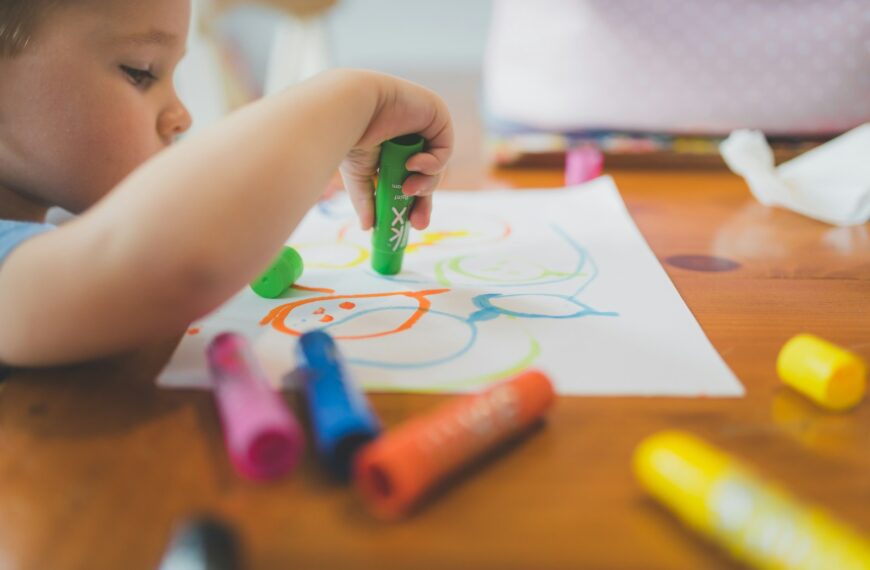 a little boy that is sitting at a table with some crayons