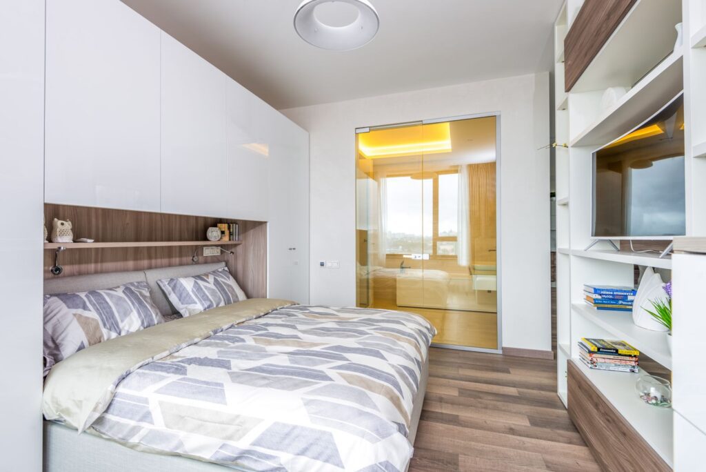Side view of contemporary cozy bedroom with bedside wardrobe and cabinets and bathroom with glass doors