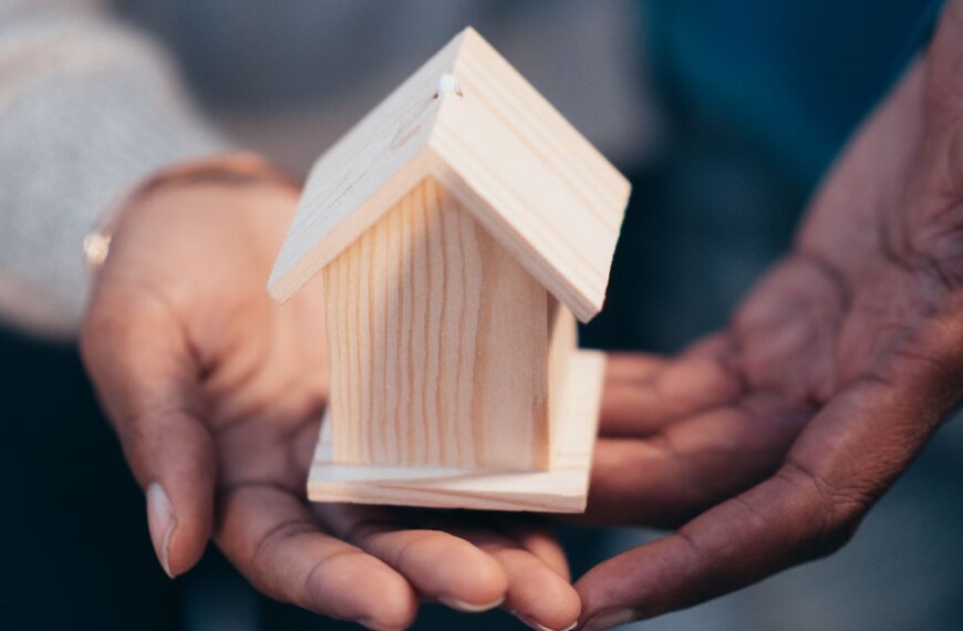 Close-up of hands holding a wooden house model representing real estate or new home purchase.