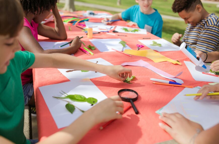 Kids engaging in fun arts and crafts, using leaves and paper outside at a colorful table.