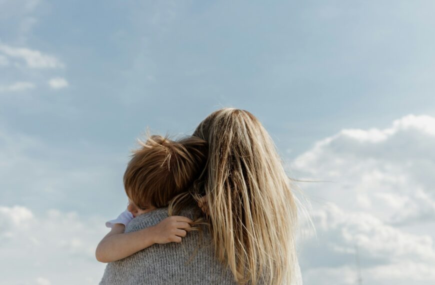 woman holding child from behind against cloudy sky