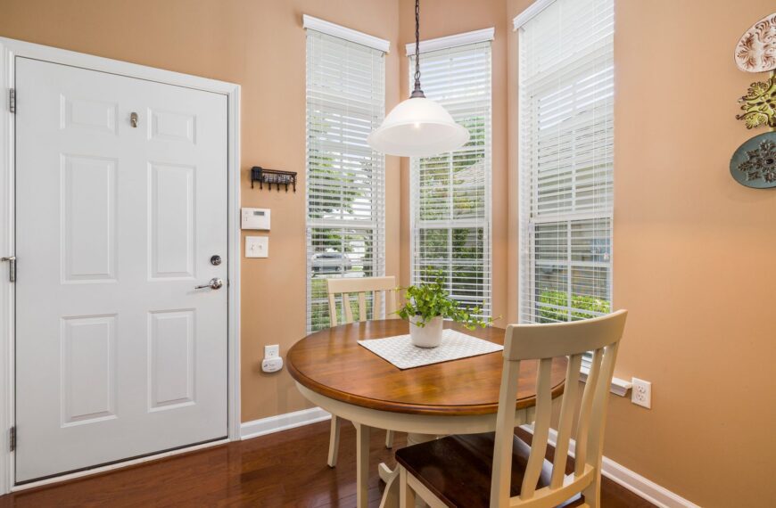 Bright dining area with round table, chairs, and houseplant by the window.