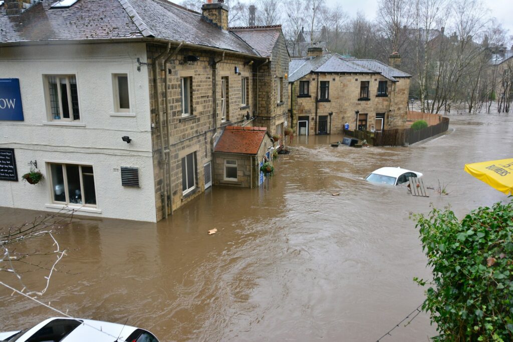 Floodwaters surrounding stone buildings and a partially submerged white car in a town