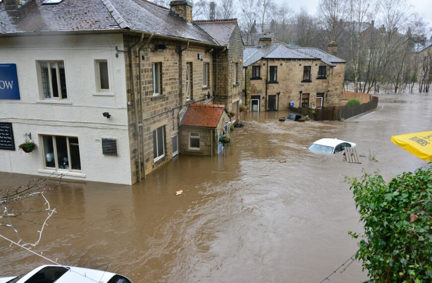 Floodwaters surrounding stone buildings and a partially submerged white car in a town