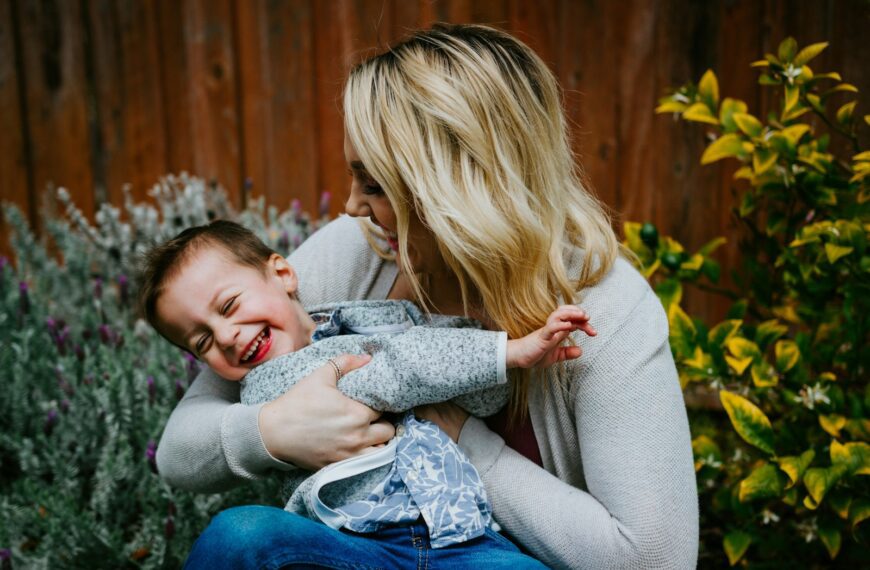 woman in gray sweater carrying girl in blue denim jacket