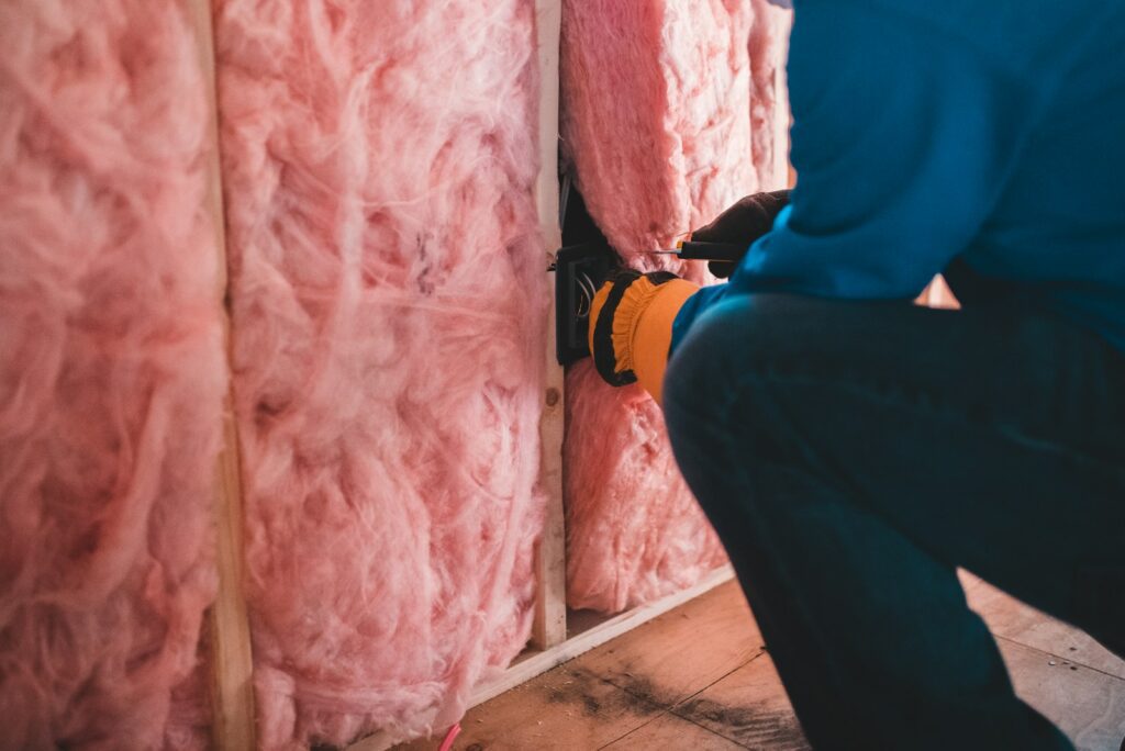 A person in a blue shirt installing electrical wiring in pink fiberglass wall insulation