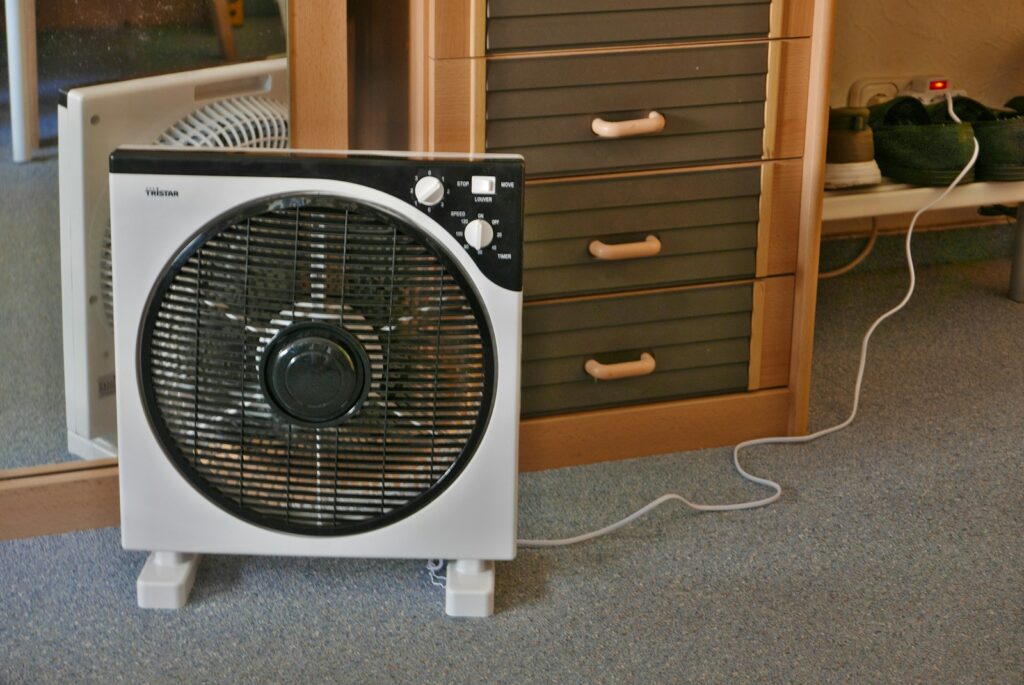 A fan is positioned near a dresser and mirror