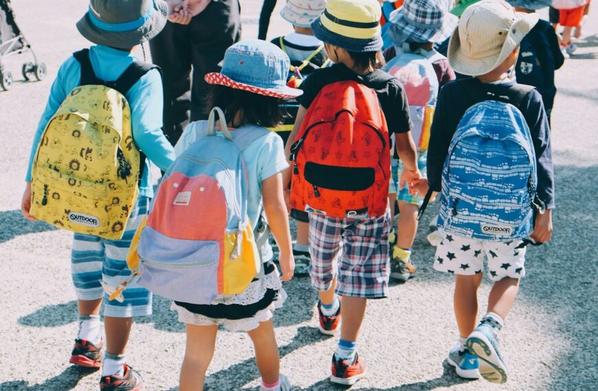 group of people wearing white and orange backpacks walking on gray concrete pavement during daytime