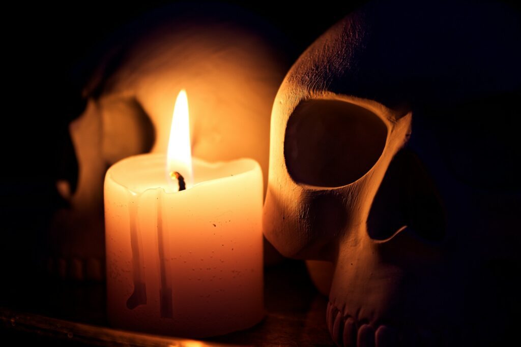 A burning candle illuminates two skulls in darkness