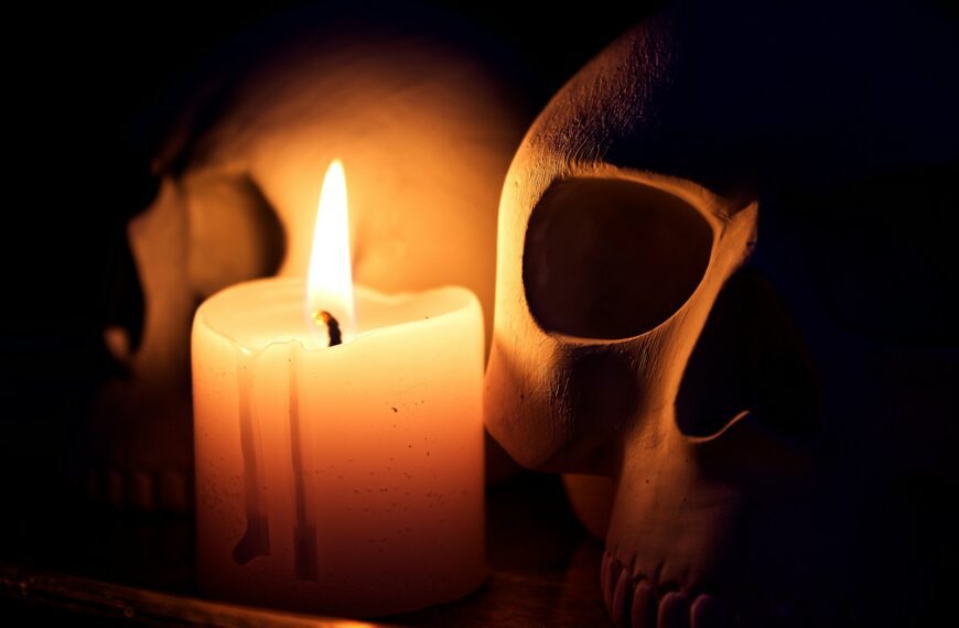 A burning candle illuminates two skulls in darkness