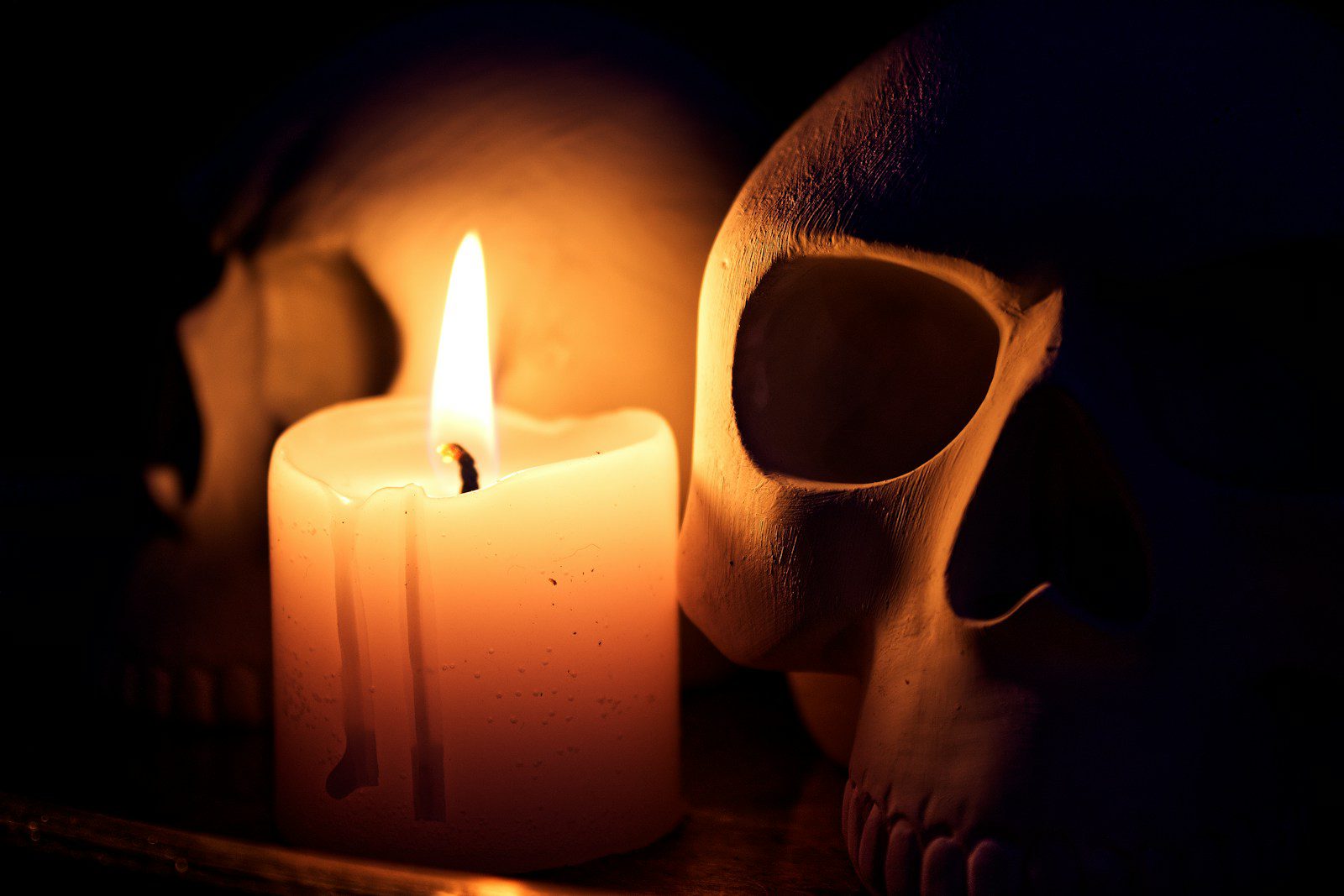 A burning candle illuminates two skulls in darkness