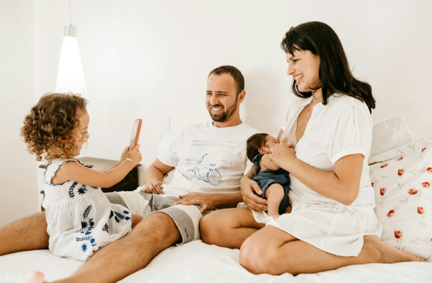 A family on a bed, a child holding a phone, an adult holding a baby