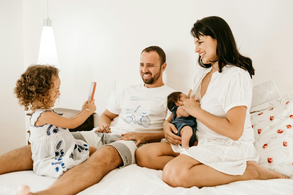 A family on a bed, a child holding a phone, an adult holding a baby