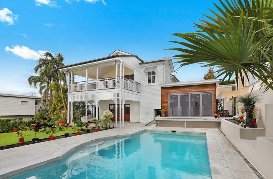 A white house with a wooden extension and a swimming pool in a garden