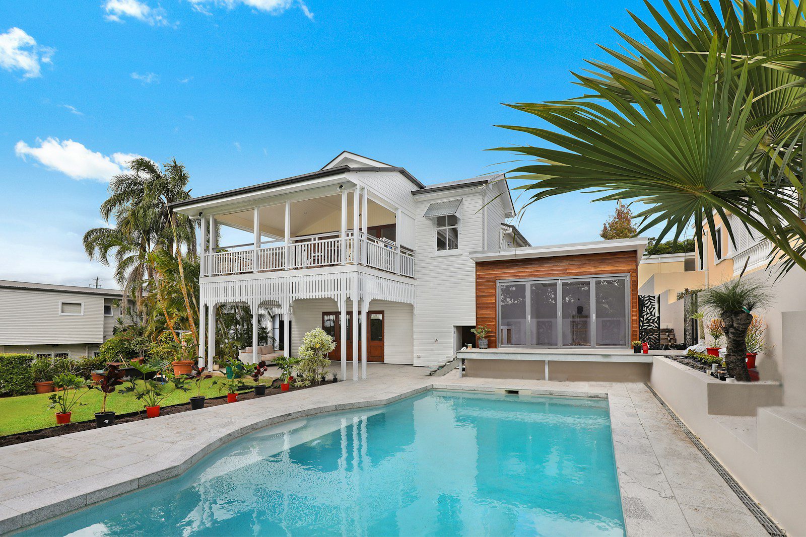 A white house with a wooden extension and a swimming pool in a garden