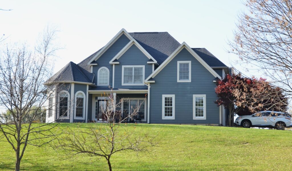 A large blue house sits on a grassy hill