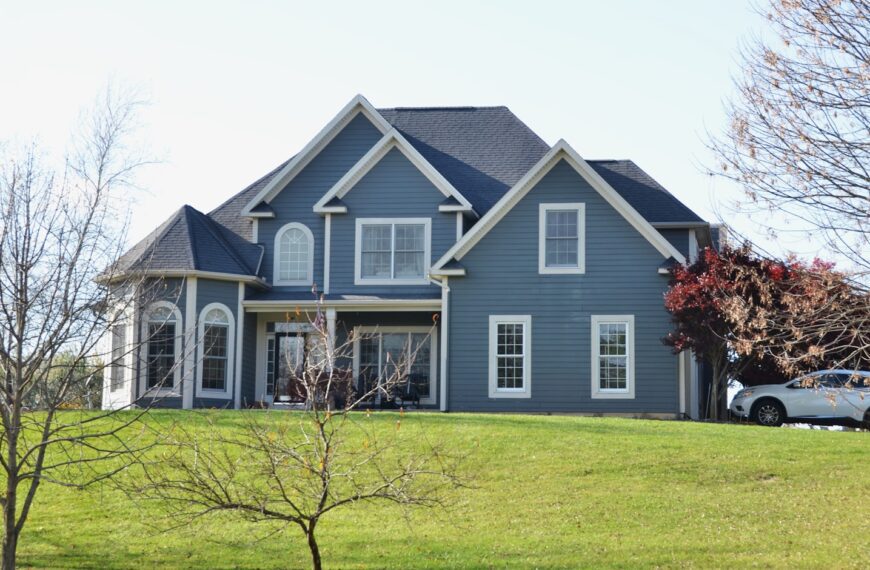 A large blue house sits on a grassy hill