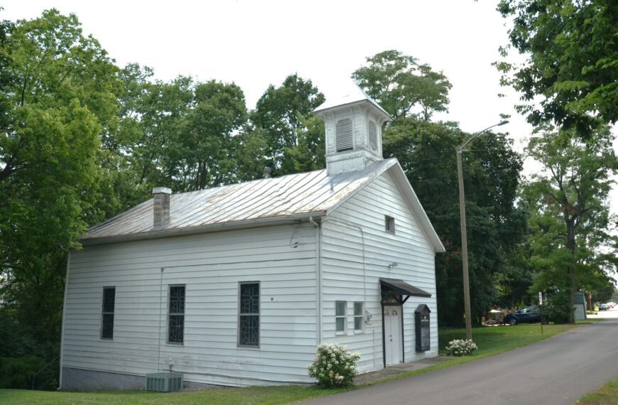 White building with a bell tower surrounded by green trees