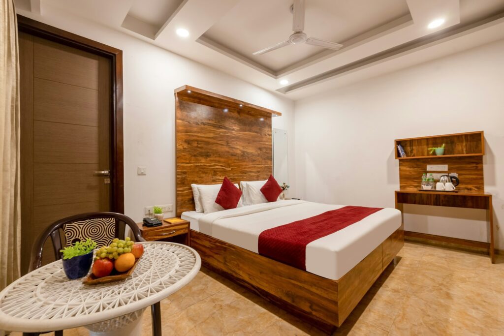 A hotel bedroom with a wooden bed frame, red accents, and a fruit bowl