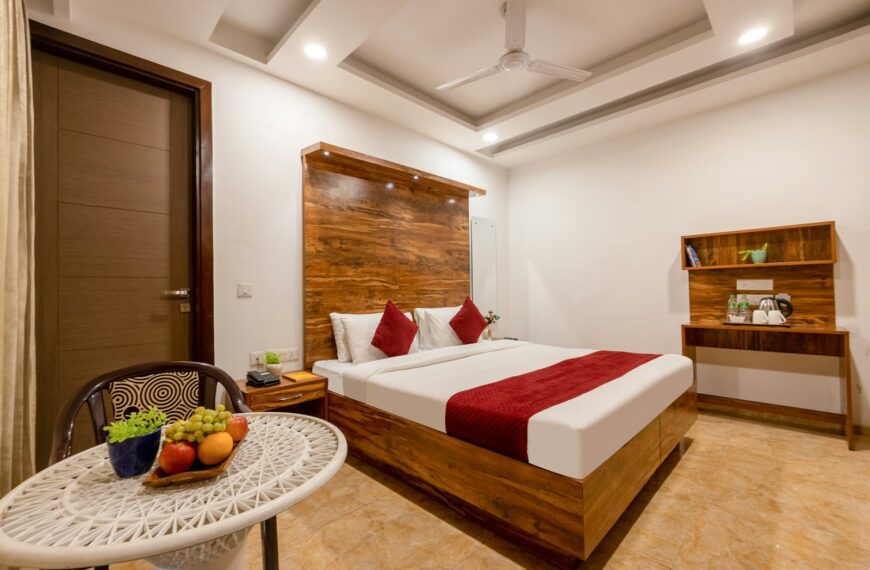 A hotel bedroom with a wooden bed frame, red accents, and a fruit bowl