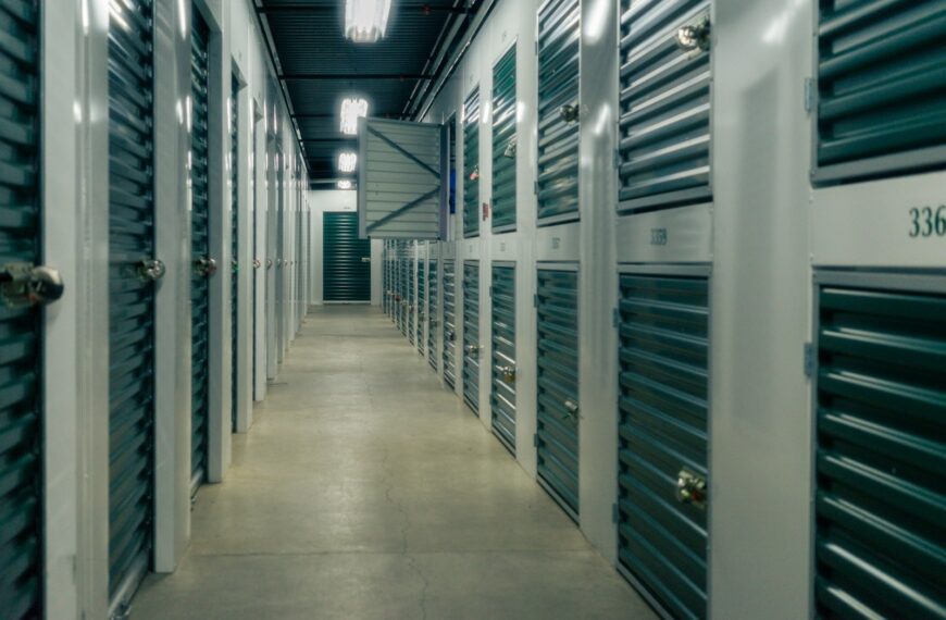 A long hallway lined with green metal storage unit doors and padlocks