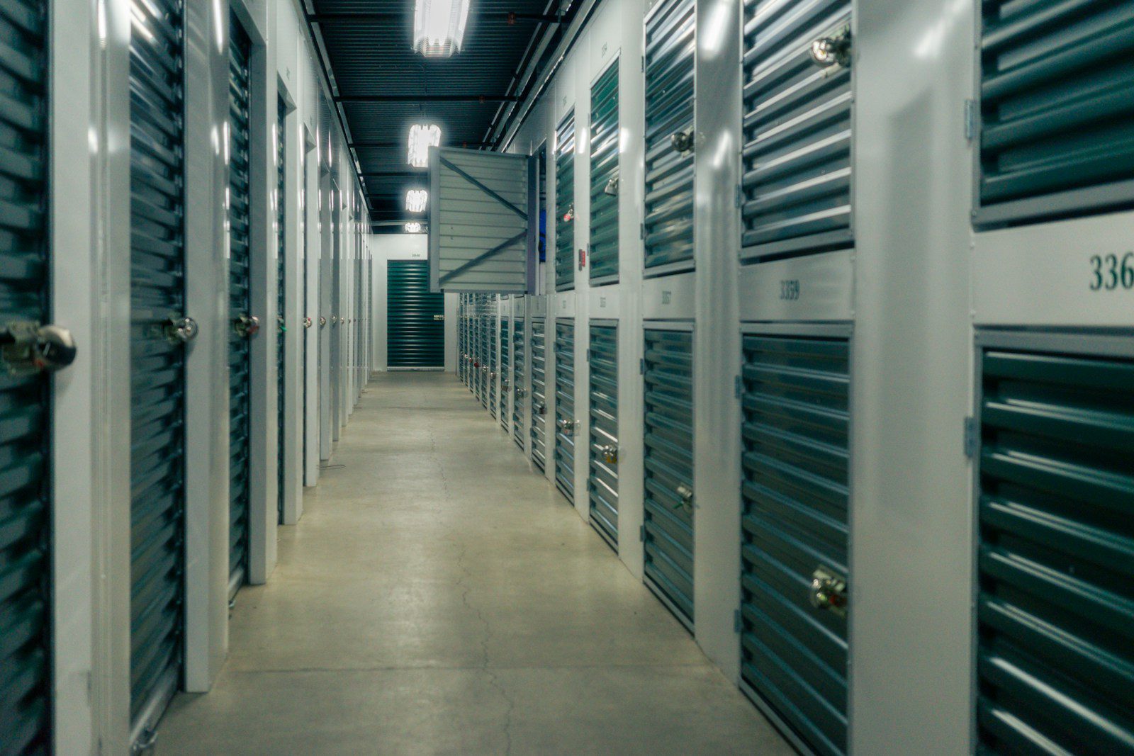 A long hallway lined with green metal storage unit doors and padlocks