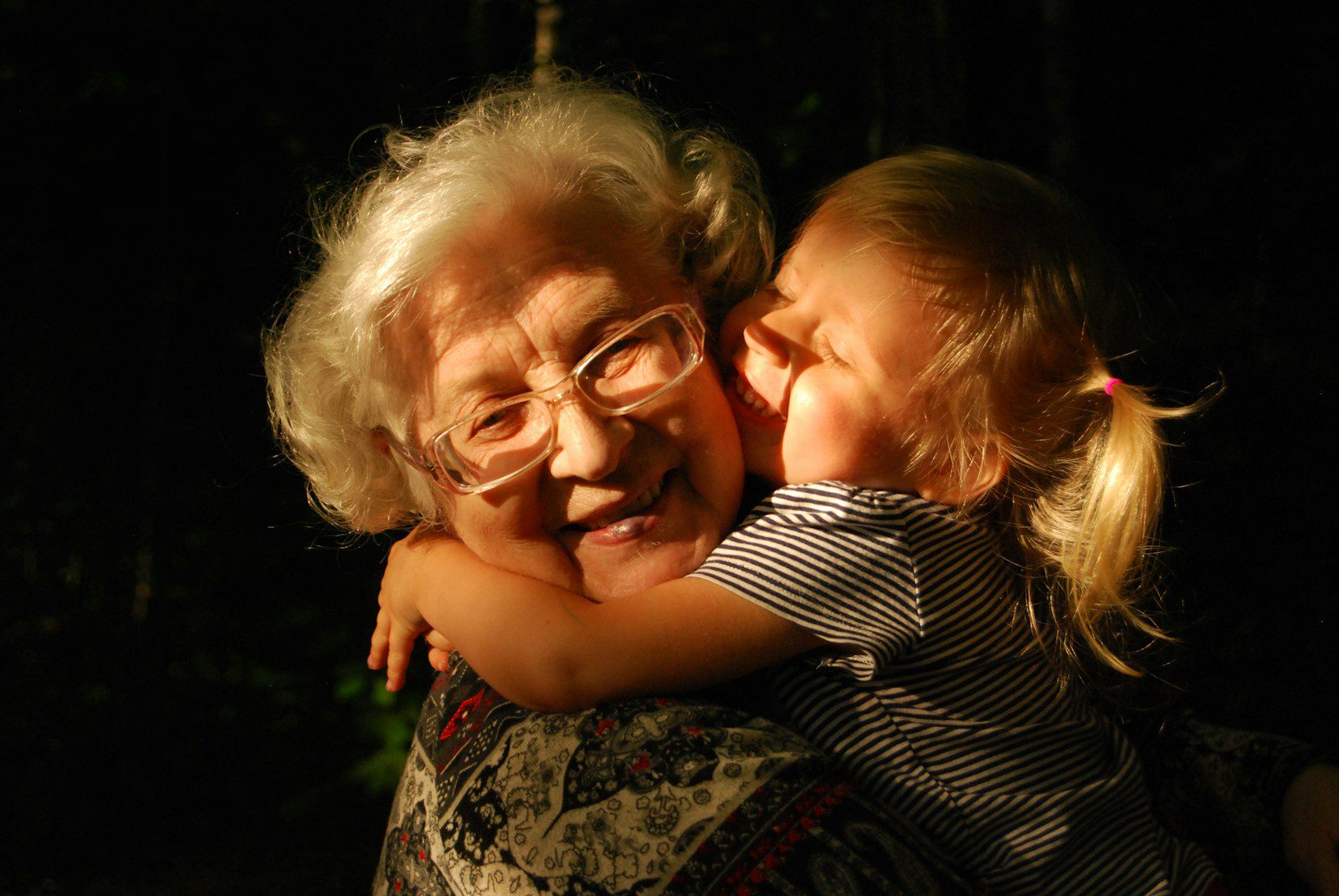 An elderly woman with white hair and glasses hugging a young child