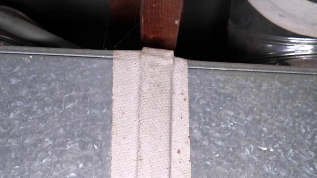 Close-up of white fibrous tape sealing a galvanized HVAC duct seam under a wooden joist, from the sprucehill.homes TikTok