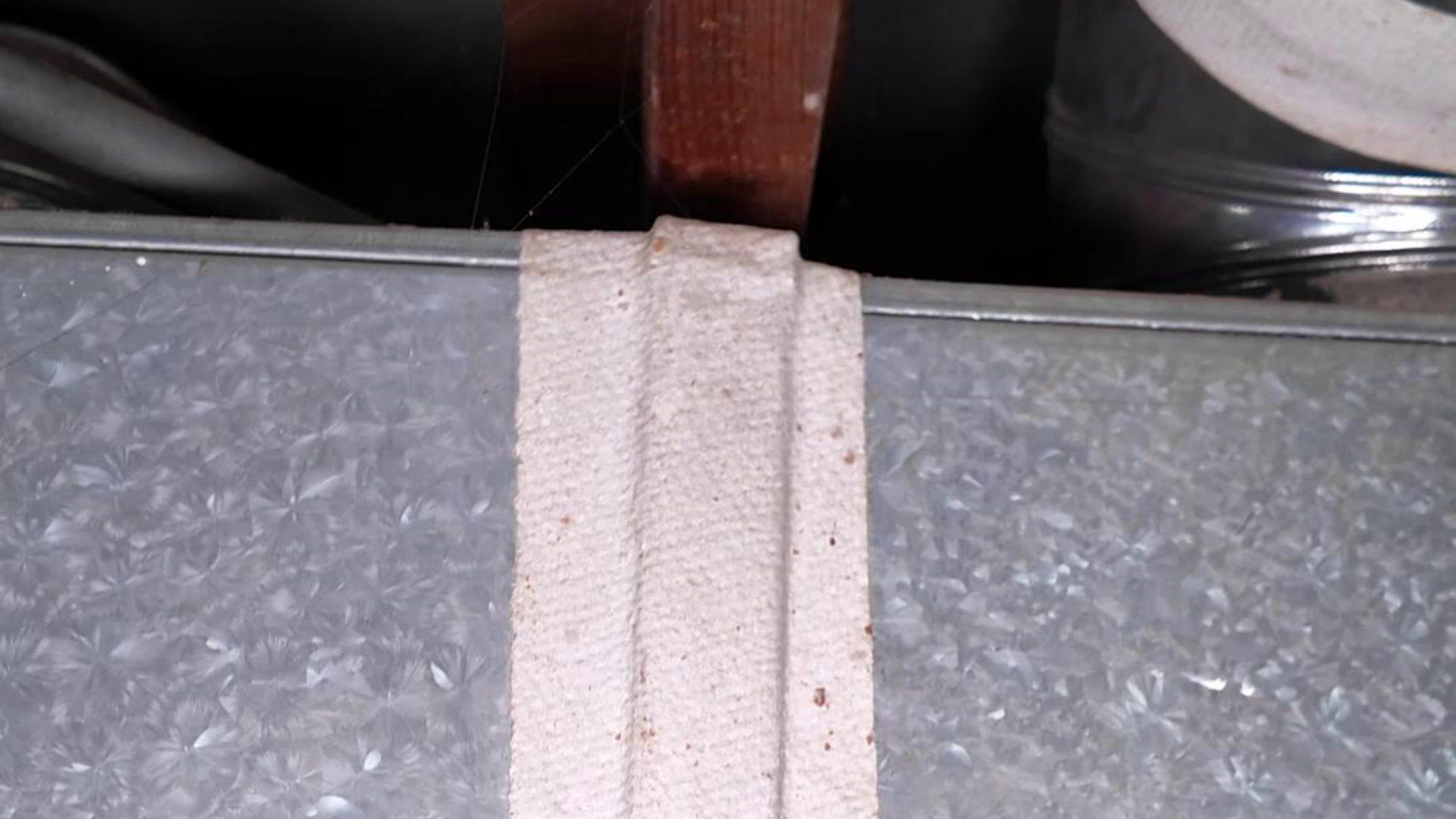 Close-up of white fibrous tape sealing a galvanized HVAC duct seam under a wooden joist, from the sprucehill.homes TikTok