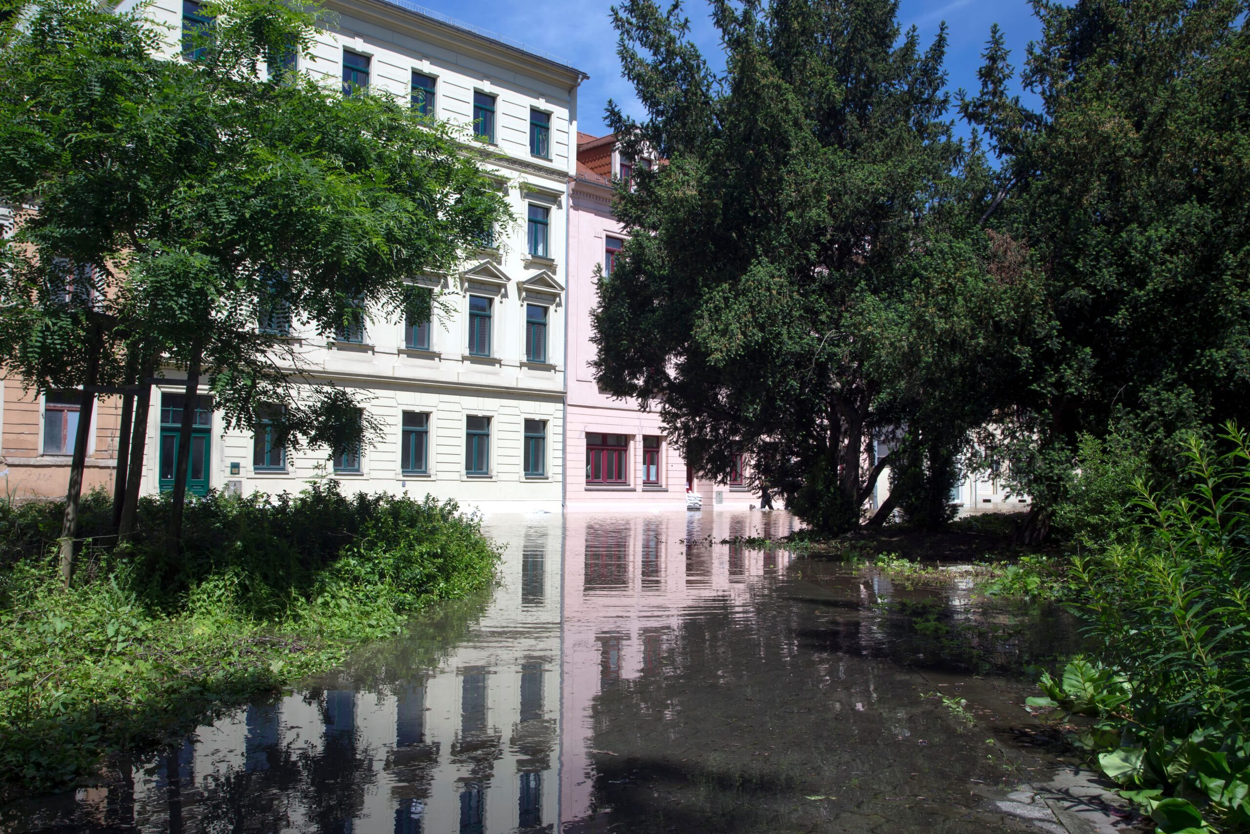 Sunlit flooded street with water pooling near buildings after heavy rain