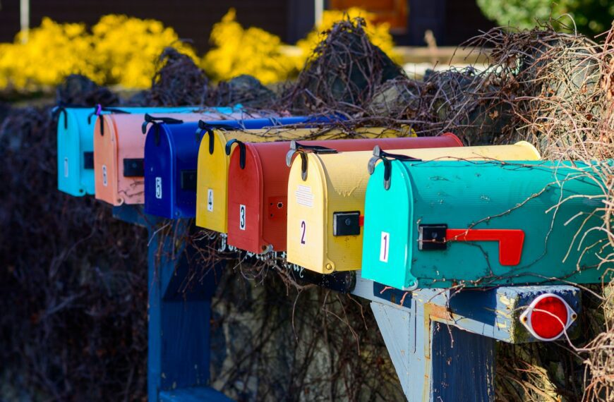 a row of colorful mail boxes sitting next to a bush