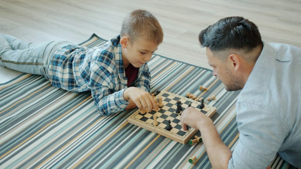 Father and son playing chess on a striped blanket