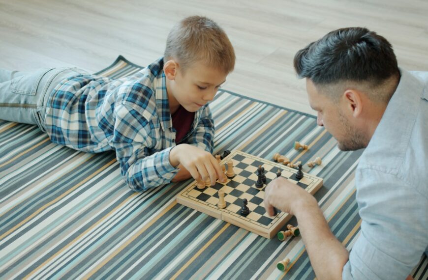 Father and son playing chess on a striped blanket