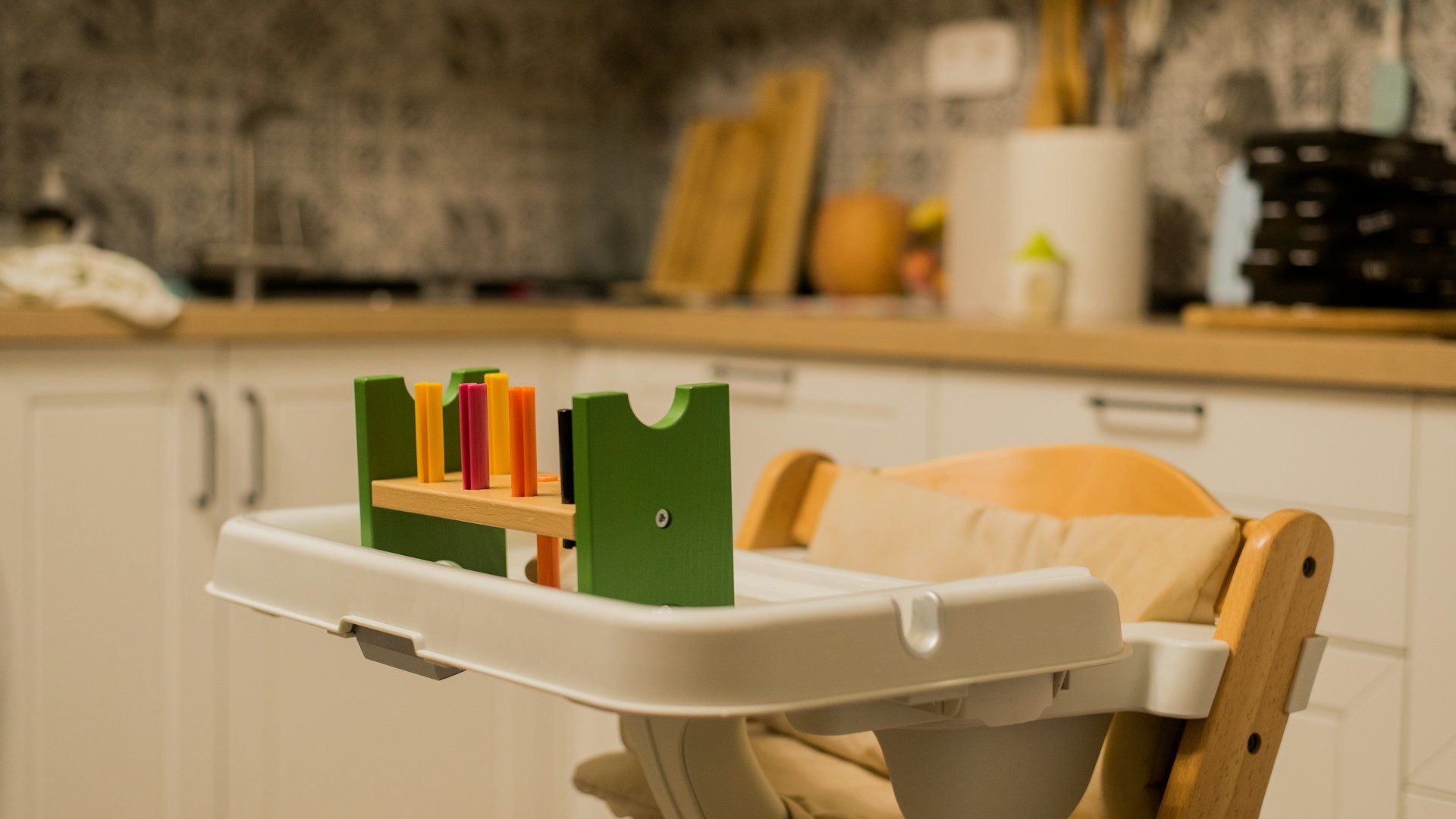 An empty child's high chair with a wooden frame and tray in a bright kitchen.