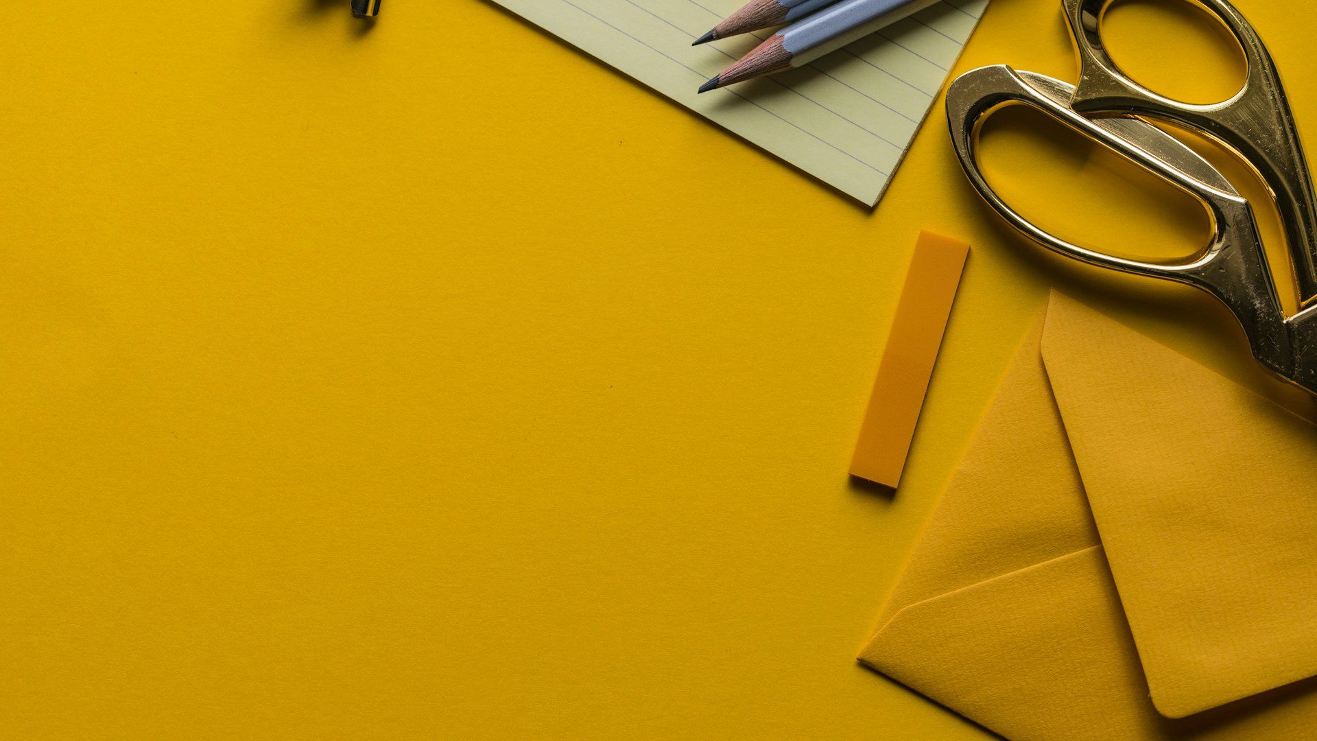 Scissors, pencils and envelopes laid out on a yellow office desk.