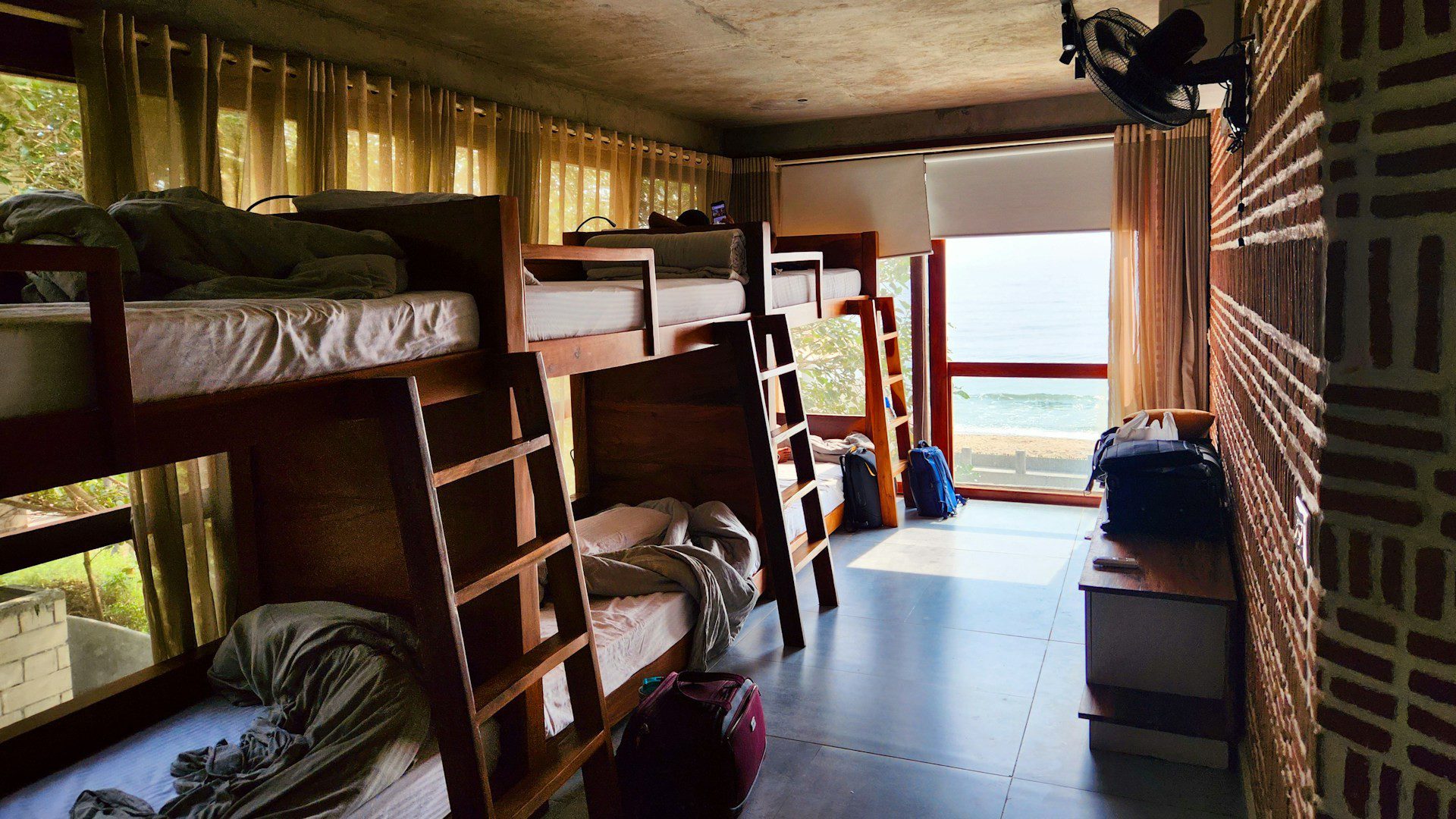 A room with several wooden bunk beds beside a large window.
