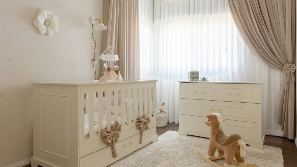 A cream-colored nursery with a white crib, dresser and plush rocking horse.