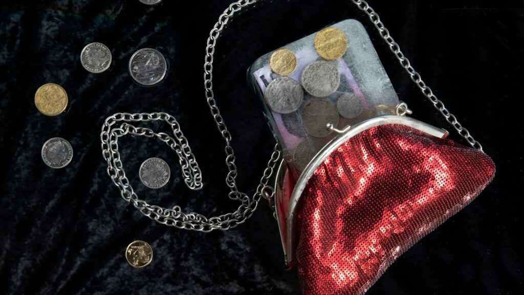 A red coin purse with a chain sits among scattered coins.