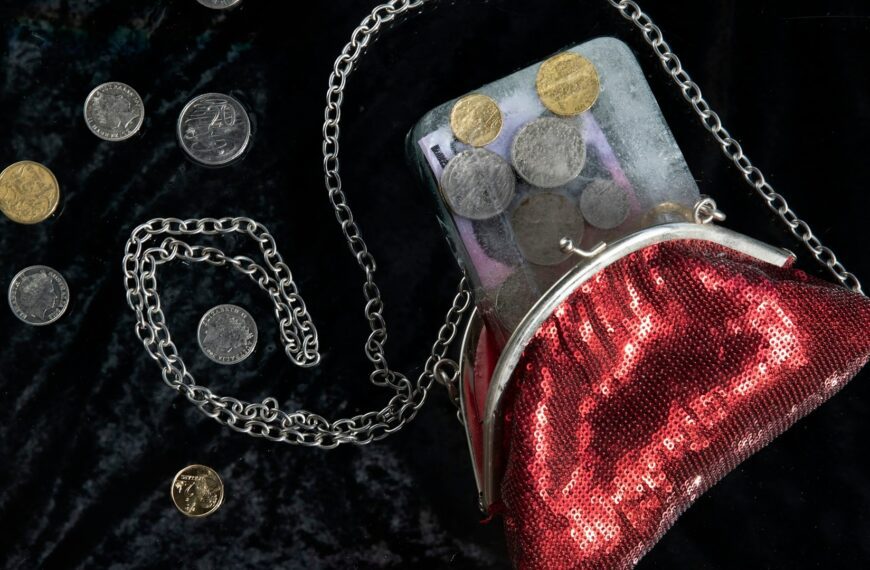 A red coin purse with a chain sits among scattered coins.