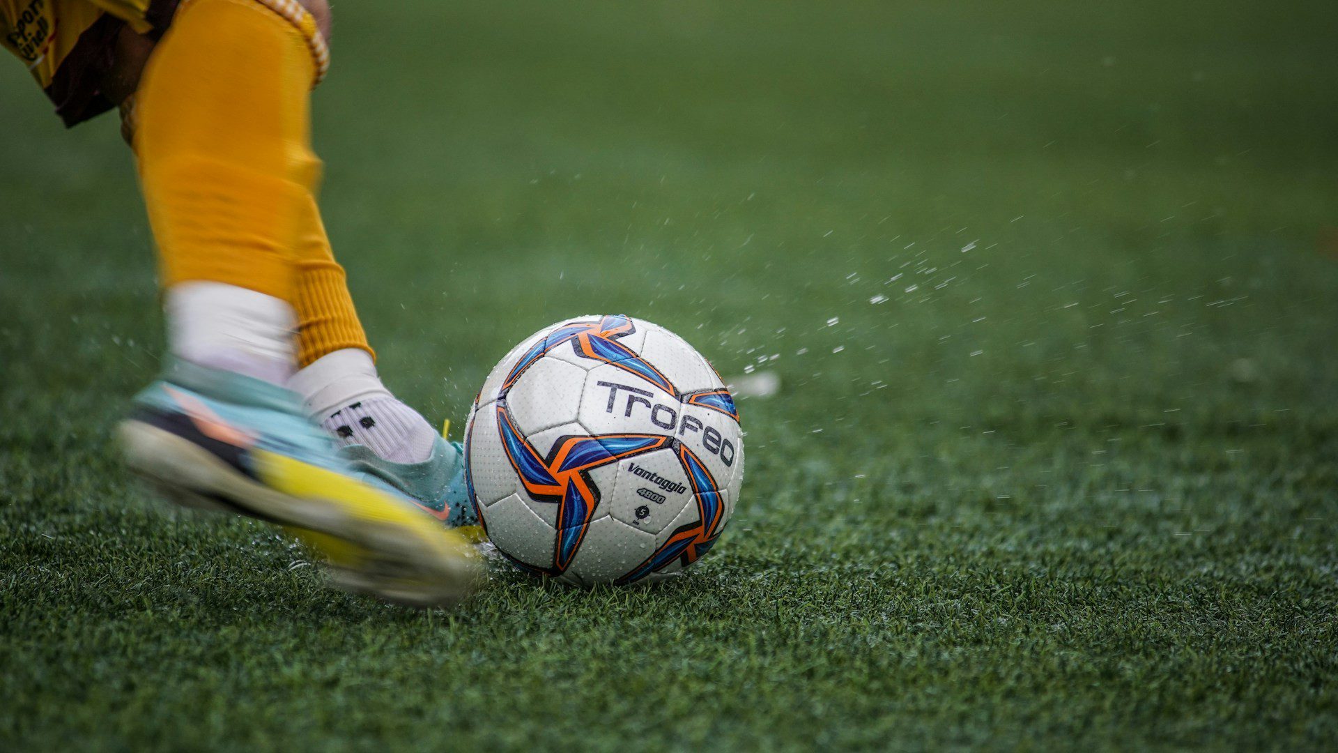 A soccer ball and cleats in motion on a green field.