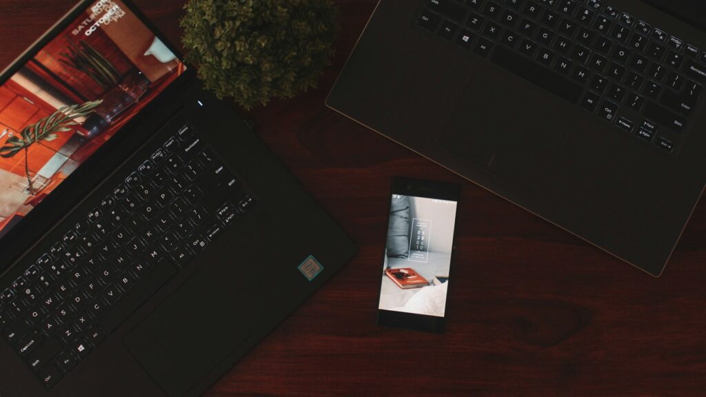 A smartphone beside open laptops on a desk.