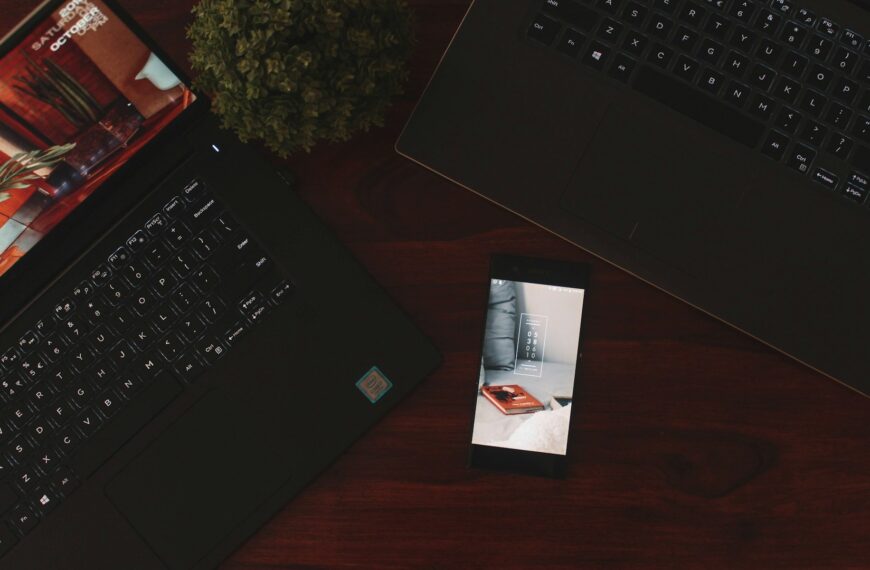 A smartphone beside open laptops on a desk.