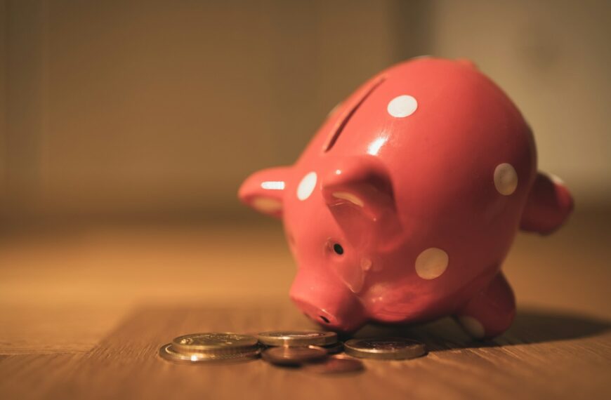A pink piggy bank with coins on a wooden table.