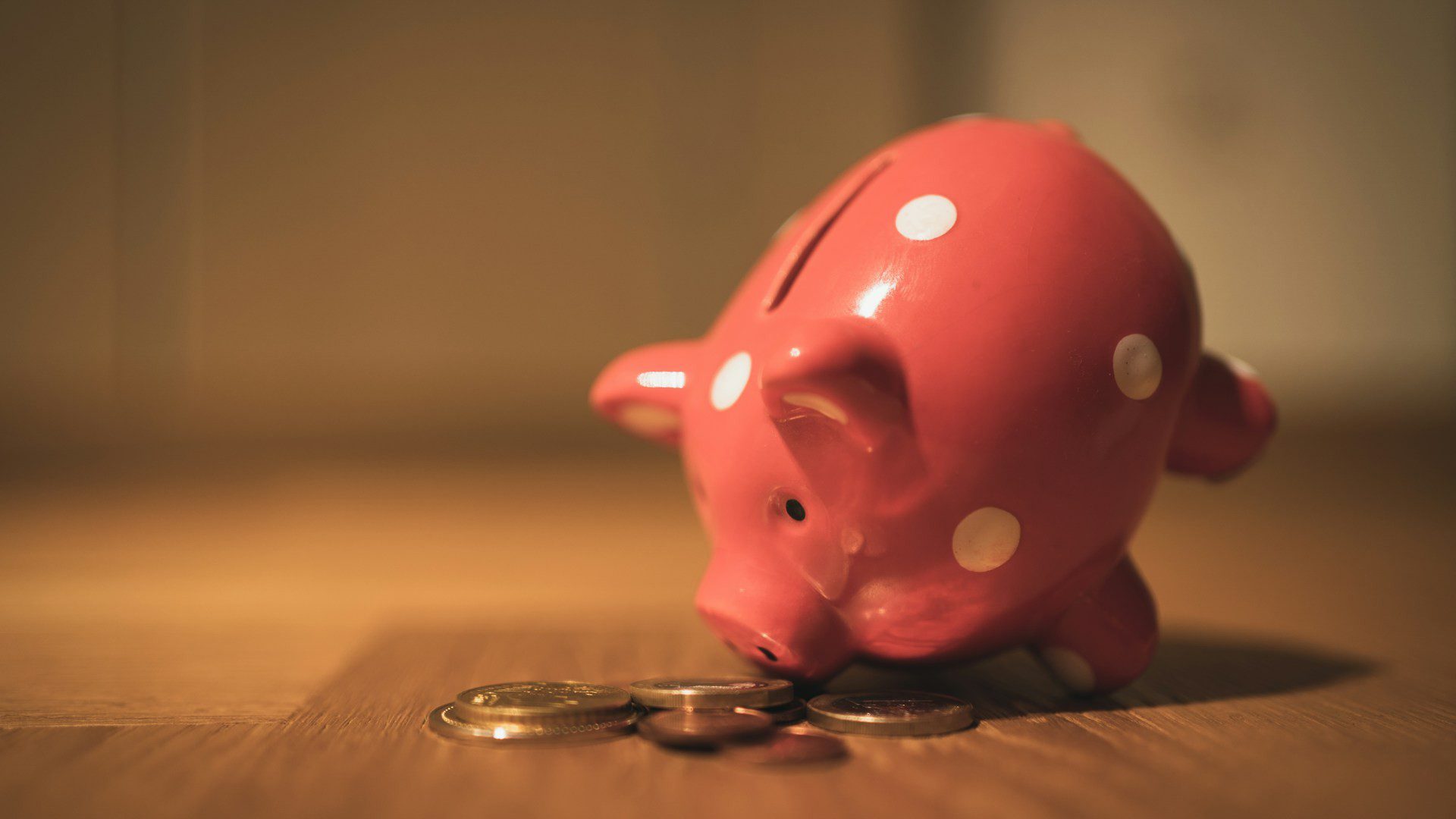 A pink piggy bank with coins on a wooden table.