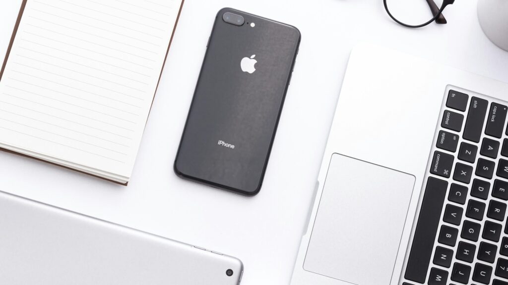 A smartphone resting beside a laptop on a desk.