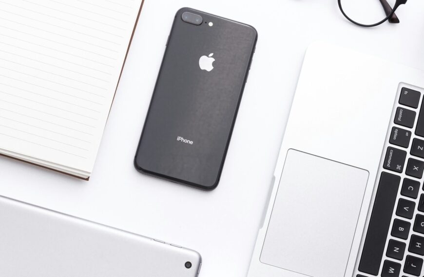 A smartphone resting beside a laptop on a desk.