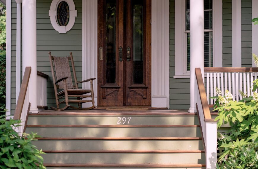 A rocking chair on a front porch beside closed doors.