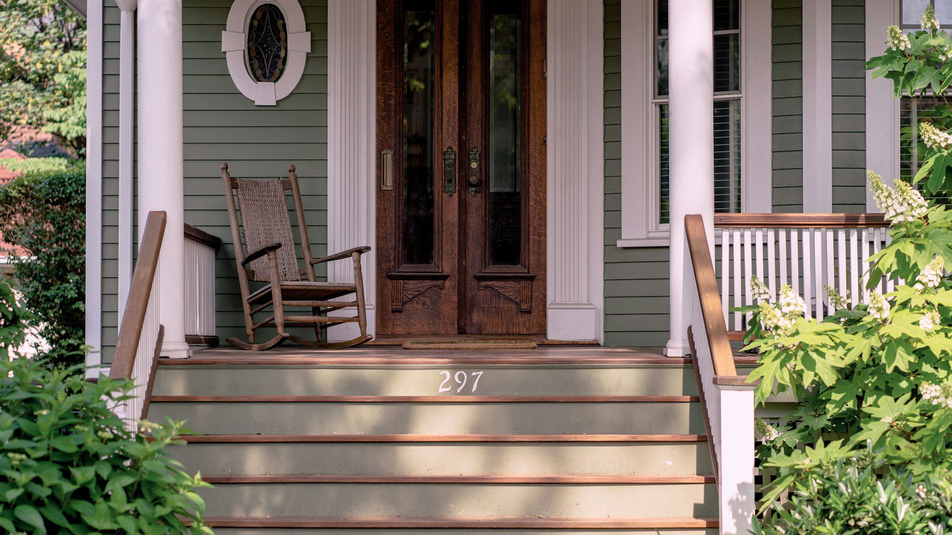 A rocking chair on a front porch beside closed doors.